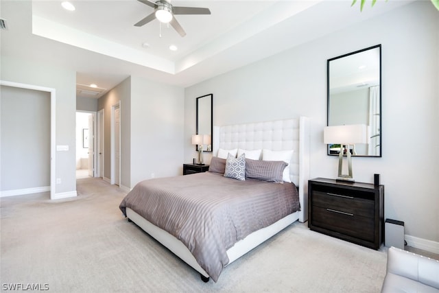 bedroom with ensuite bath, a tray ceiling, ceiling fan, and light carpet