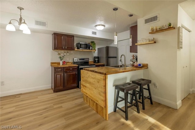 kitchen with hanging light fixtures, stainless steel appliances, a kitchen breakfast bar, light hardwood / wood-style flooring, and kitchen peninsula