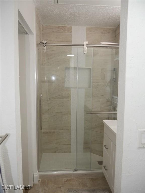 full bath featuring a textured ceiling, a shower stall, and vanity