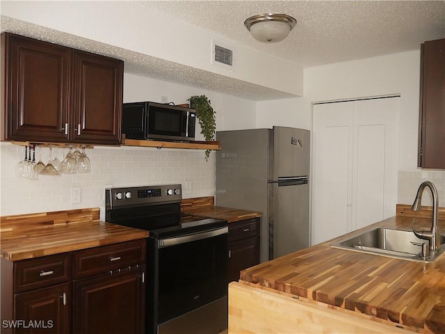 kitchen with decorative backsplash, a sink, appliances with stainless steel finishes, visible vents, and butcher block countertops