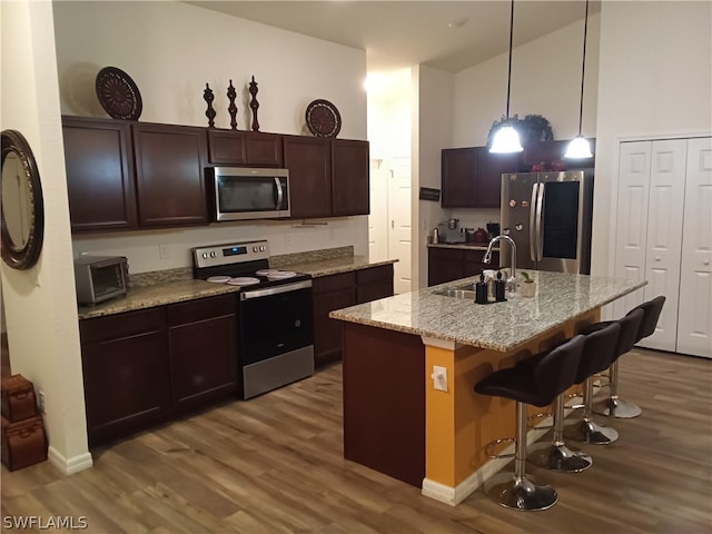 kitchen with pendant lighting, stainless steel appliances, a kitchen bar, hardwood / wood-style floors, and sink