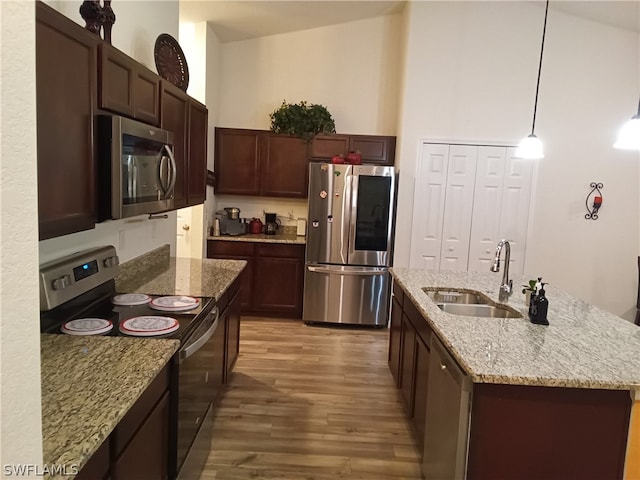 kitchen featuring stainless steel appliances, decorative light fixtures, light stone countertops, hardwood / wood-style floors, and a center island with sink