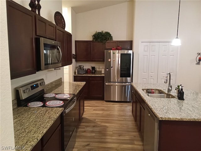 kitchen with light stone countertops, hardwood / wood-style floors, appliances with stainless steel finishes, sink, and pendant lighting