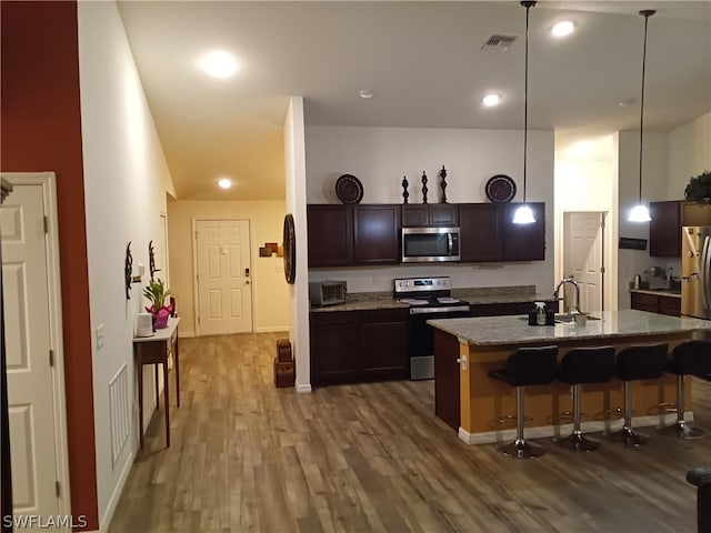 kitchen with appliances with stainless steel finishes, decorative light fixtures, stone counters, and dark hardwood / wood-style flooring