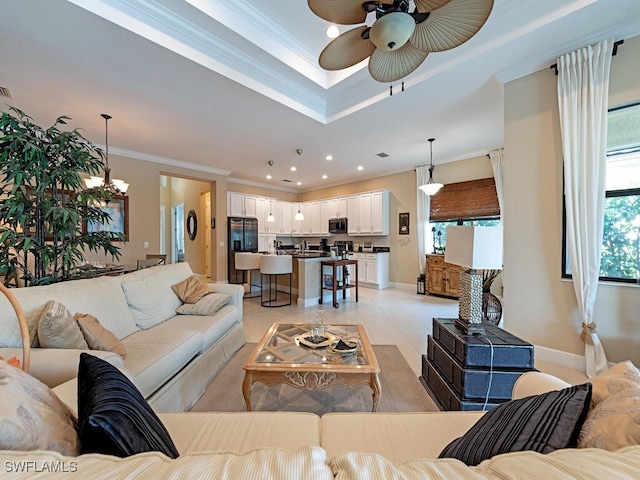 tiled living room with ceiling fan with notable chandelier, a raised ceiling, and crown molding