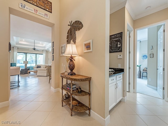 hallway featuring a tray ceiling, crown molding, and light tile patterned floors