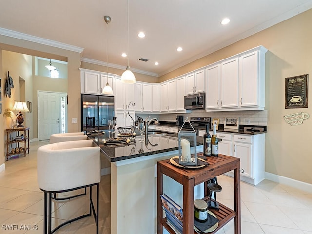 kitchen with a kitchen island with sink, tasteful backsplash, appliances with stainless steel finishes, a breakfast bar area, and white cabinets