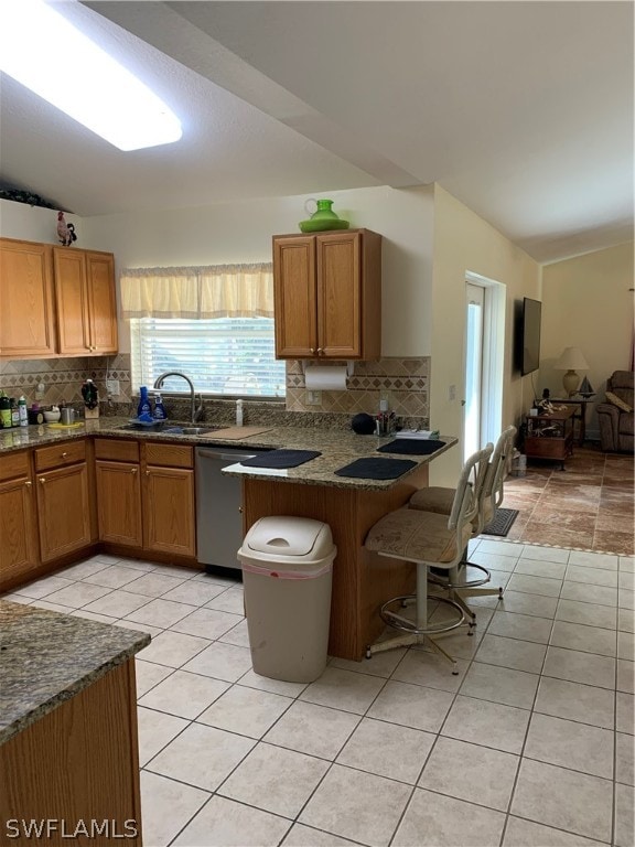 kitchen with kitchen peninsula, light tile floors, a kitchen breakfast bar, dishwasher, and backsplash