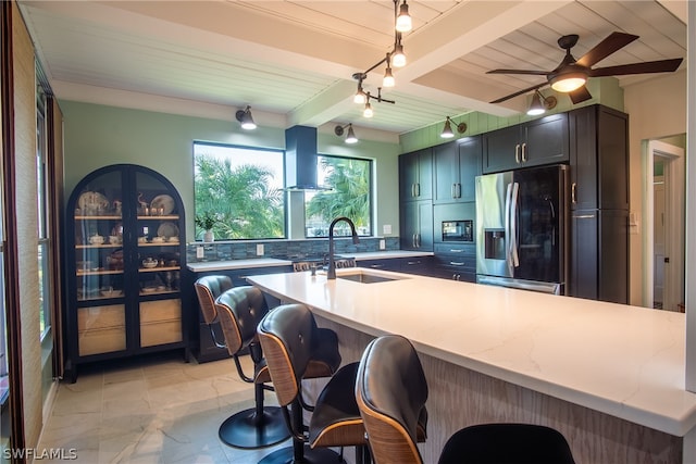 kitchen featuring ceiling fan, stainless steel fridge, black microwave, beam ceiling, and wall chimney range hood