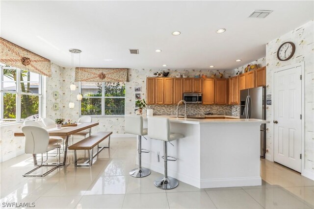 kitchen featuring a breakfast bar, decorative light fixtures, backsplash, light tile patterned floors, and stainless steel appliances