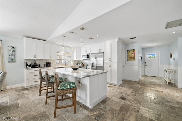 kitchen with white cabinetry, decorative light fixtures, appliances with stainless steel finishes, a kitchen island, and decorative backsplash