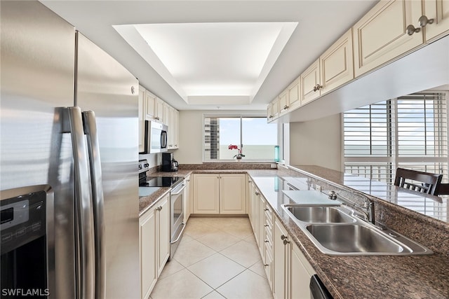 kitchen featuring a tray ceiling, stainless steel appliances, light tile floors, and cream cabinets