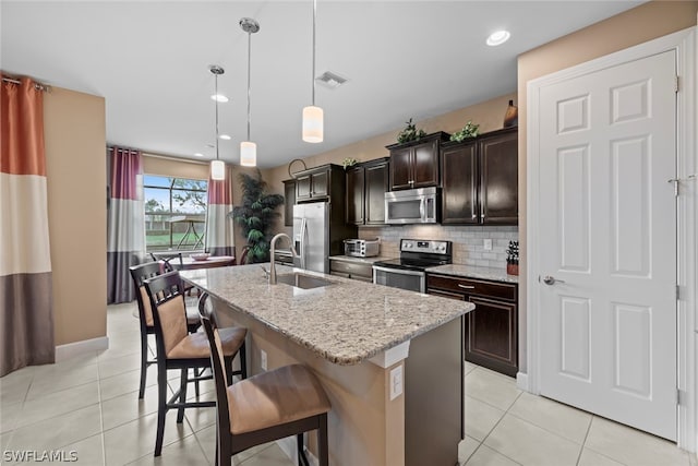 kitchen with a kitchen island with sink, sink, hanging light fixtures, backsplash, and stainless steel appliances