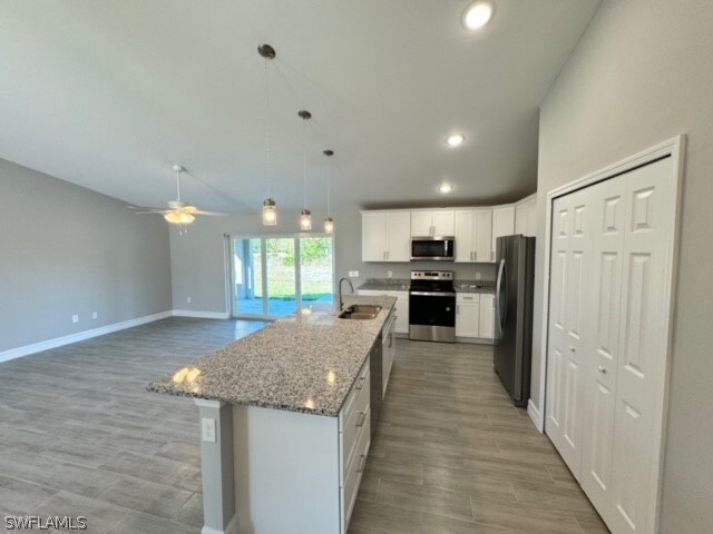 kitchen featuring stainless steel appliances, ceiling fan, a kitchen island with sink, white cabinets, and sink