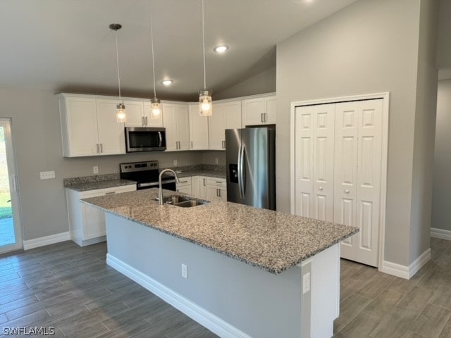 kitchen with a center island with sink, pendant lighting, sink, lofted ceiling, and appliances with stainless steel finishes