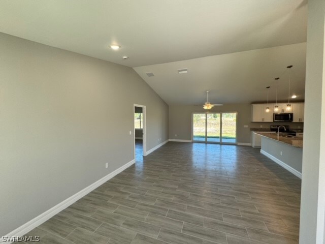 unfurnished living room with sink, ceiling fan, light tile floors, and lofted ceiling