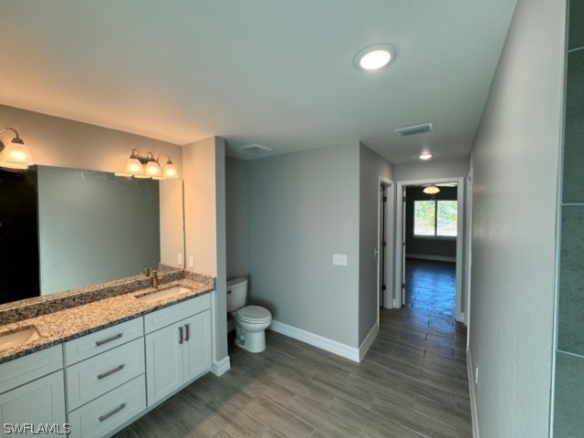 bathroom featuring dual sinks, toilet, and vanity with extensive cabinet space