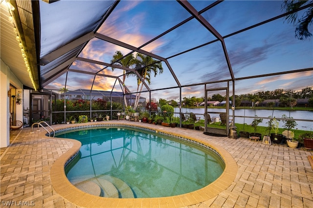 pool at dusk featuring glass enclosure, a water view, and a patio