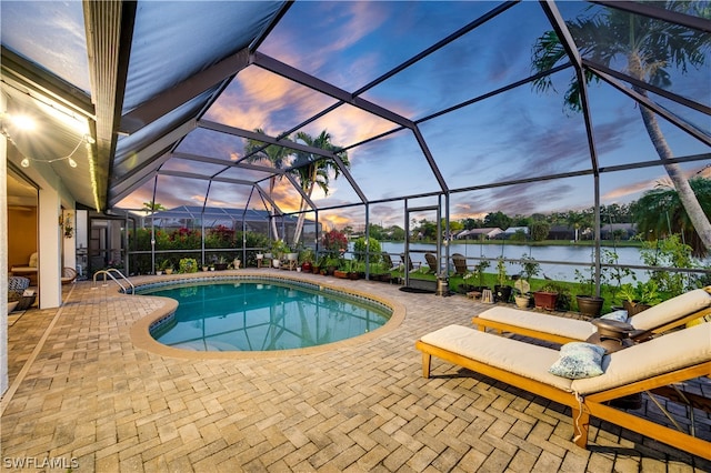 pool at dusk with a lanai, a patio area, and a water view