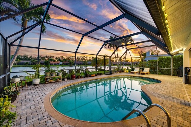 pool at dusk featuring a patio, a water view, and a lanai