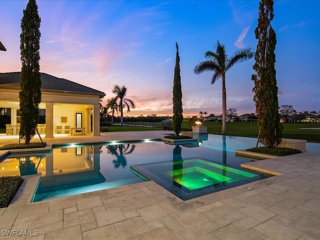 pool at dusk featuring a patio area and an in ground hot tub