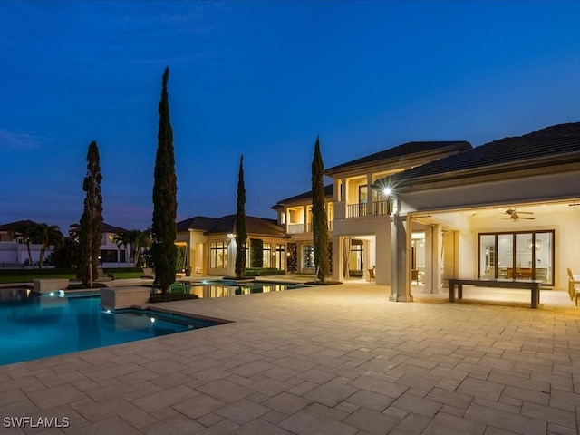 pool at dusk with a patio area and ceiling fan