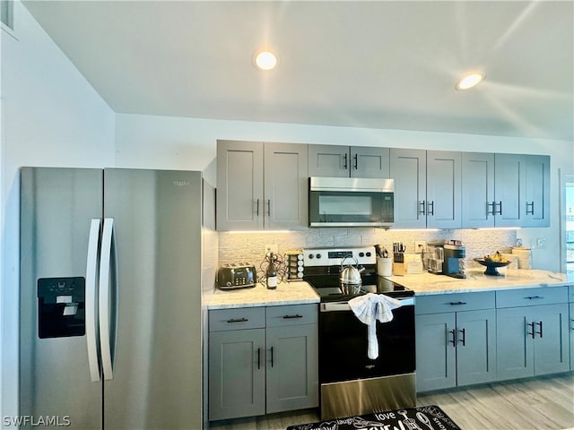 kitchen with appliances with stainless steel finishes, tasteful backsplash, light stone counters, and light hardwood / wood-style flooring