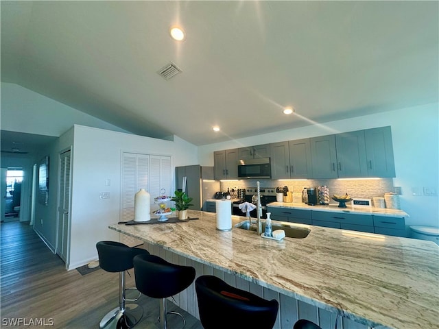 kitchen featuring backsplash, dark wood-type flooring, sink, stainless steel appliances, and a breakfast bar area