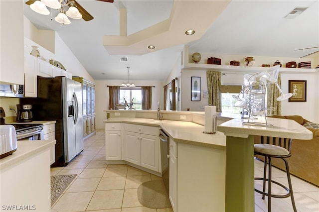 kitchen featuring appliances with stainless steel finishes, a breakfast bar, decorative light fixtures, white cabinets, and light tile patterned flooring