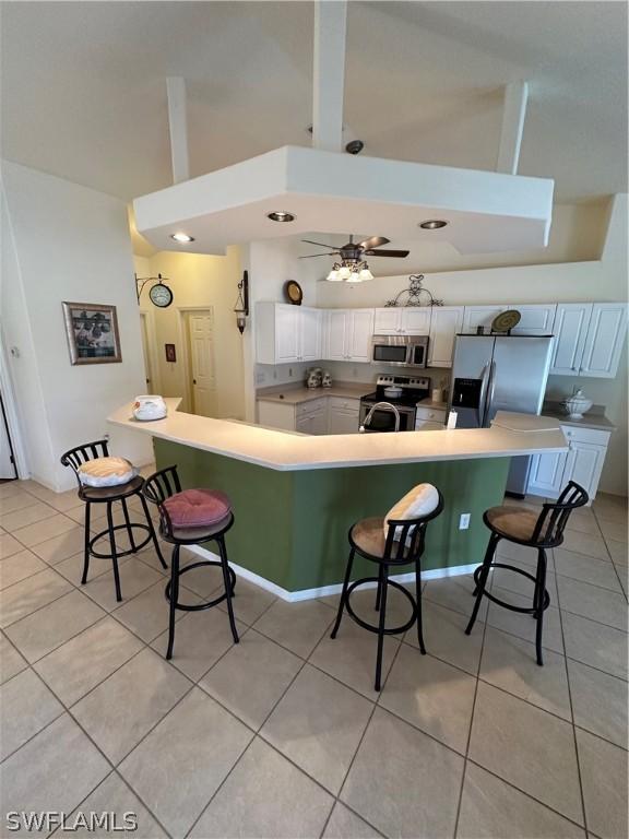 kitchen with high vaulted ceiling, white cabinets, light tile patterned flooring, a kitchen bar, and stainless steel appliances