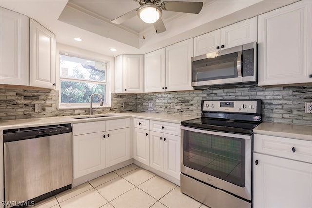 kitchen featuring ceiling fan, appliances with stainless steel finishes, white cabinets, a tray ceiling, and sink