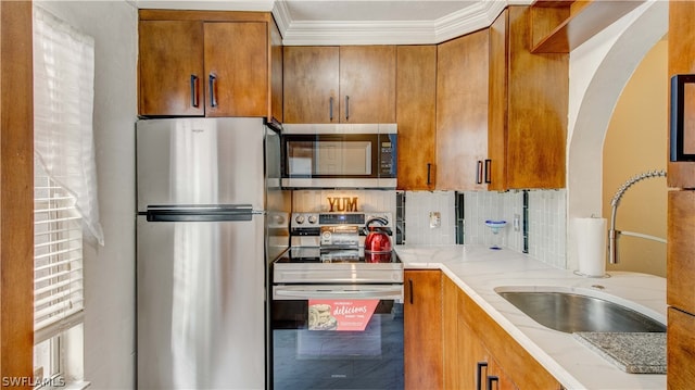 kitchen featuring backsplash, sink, stainless steel appliances, light stone counters, and ornamental molding