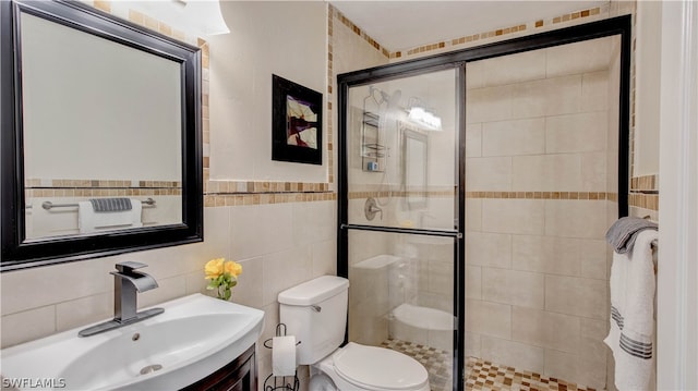 bathroom featuring tile walls, toilet, vanity with extensive cabinet space, a shower with door, and tasteful backsplash