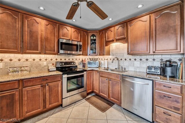 kitchen with ceiling fan, light tile floors, sink, stainless steel appliances, and light stone countertops