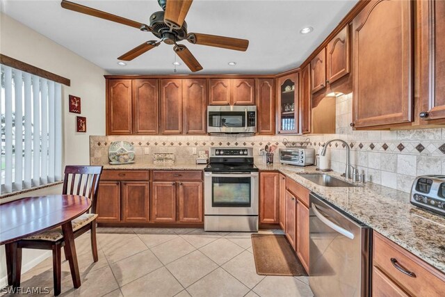 kitchen featuring ceiling fan, sink, stainless steel appliances, light tile floors, and light stone counters