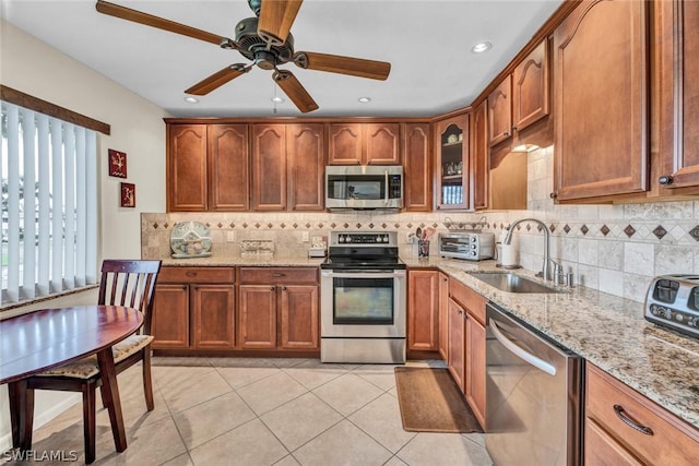 kitchen featuring stainless steel appliances, light tile patterned flooring, sink, and light stone counters