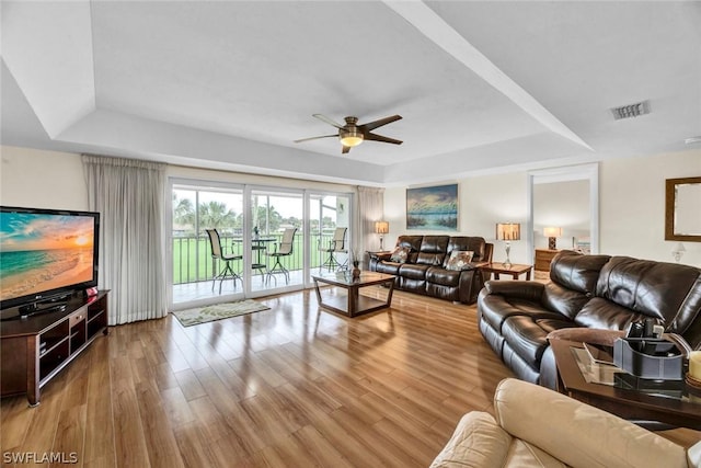 living room with a raised ceiling, wood-type flooring, and ceiling fan