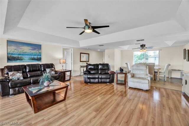 living room with light hardwood / wood-style floors, ceiling fan, and a tray ceiling