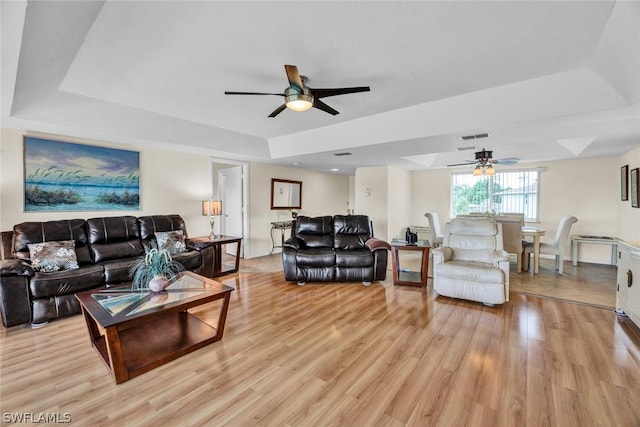 living room featuring ceiling fan, a raised ceiling, and light wood-type flooring