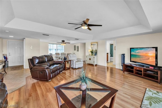 living room featuring ceiling fan, light hardwood / wood-style floors, and a tray ceiling