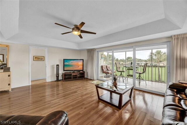 living room with plenty of natural light, a raised ceiling, ceiling fan, and wood-type flooring