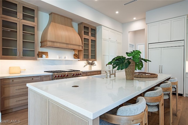 kitchen with a large island with sink, custom exhaust hood, sink, and stainless steel range oven