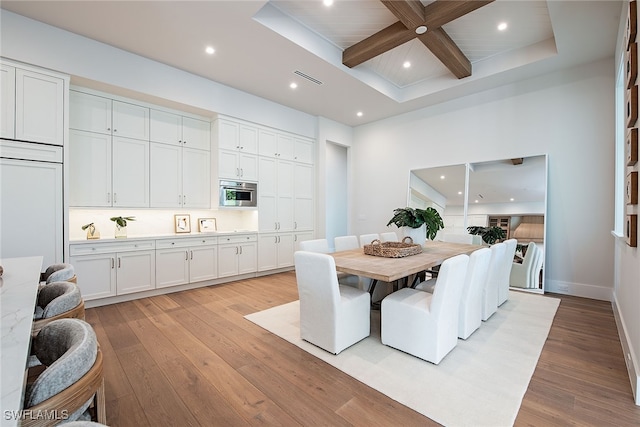 dining area featuring a towering ceiling, light wood-type flooring, beamed ceiling, and a raised ceiling