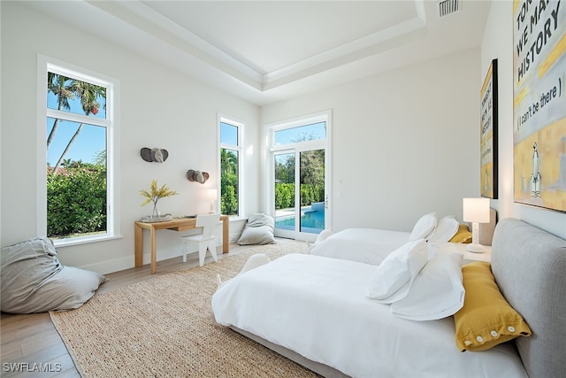 bedroom featuring wood-type flooring, multiple windows, a tray ceiling, and access to outside