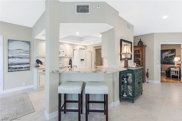 kitchen featuring kitchen peninsula, white appliances, light tile floors, light stone counters, and a raised ceiling