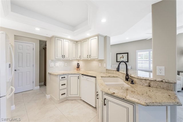 kitchen with a raised ceiling, white appliances, sink, and light stone counters