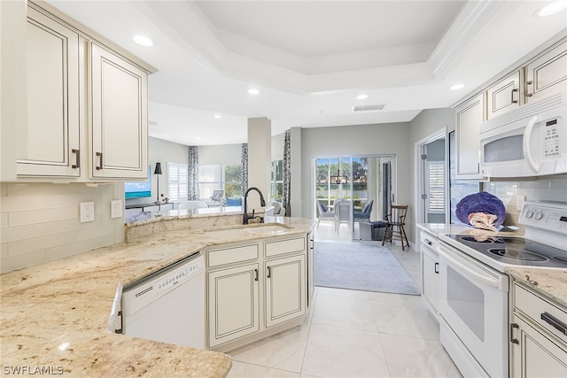 kitchen with white appliances, light stone counters, a tray ceiling, and sink