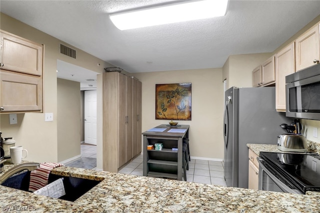 kitchen with light brown cabinets, light tile patterned flooring, a textured ceiling, and appliances with stainless steel finishes