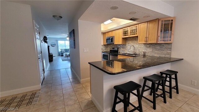 kitchen with dark stone counters, kitchen peninsula, sink, appliances with stainless steel finishes, and a breakfast bar area