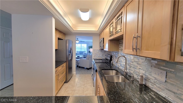 kitchen with dark stone counters, stainless steel appliances, sink, ceiling fan, and a raised ceiling